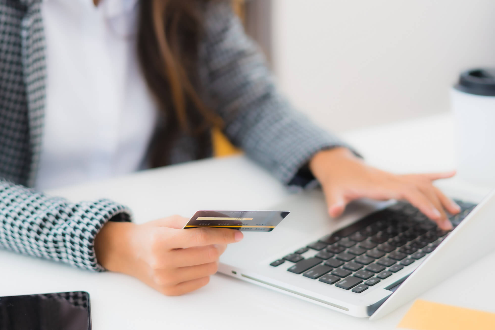 Person holding a credit card and using a laptop keyboard at a white desk.