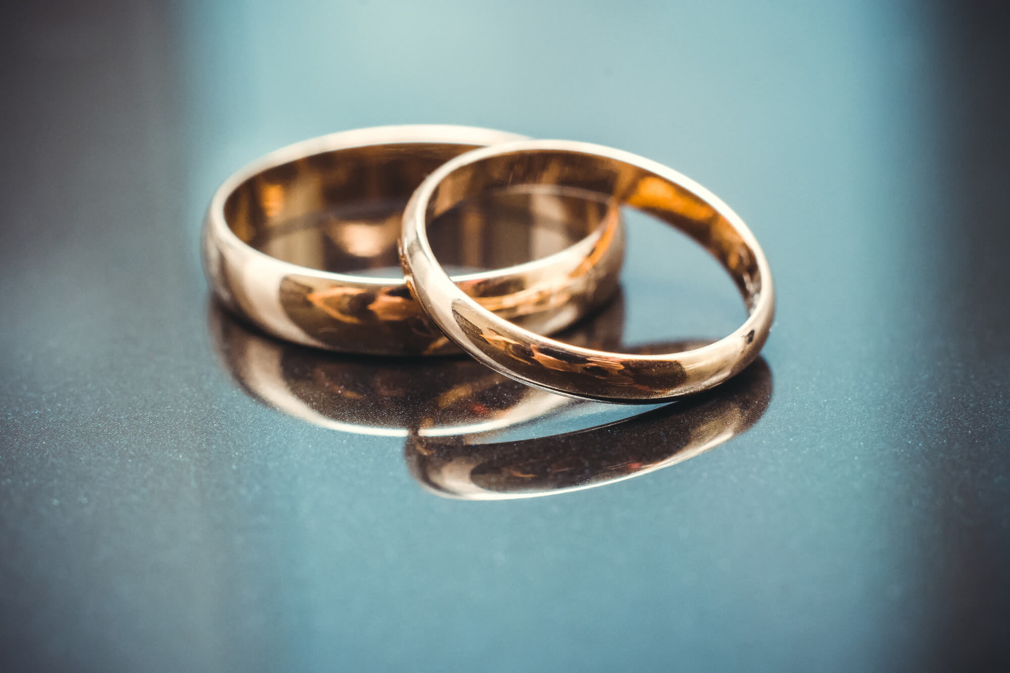Two gold wedding bands resting on a reflective dark surface with soft lighting.