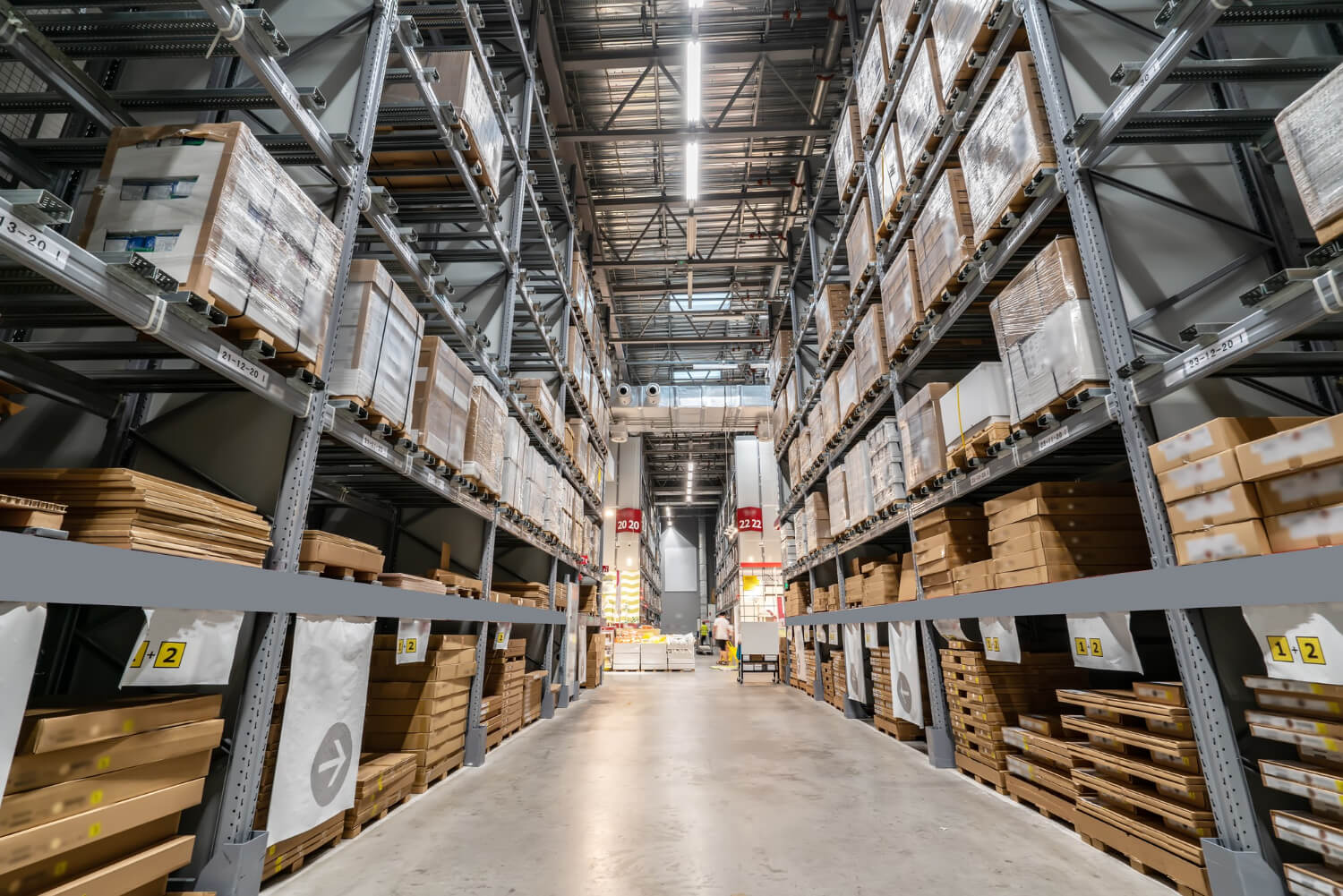 Wide aisle inside a large warehouse with tall shelves stacked with packaged boxes and pallets.