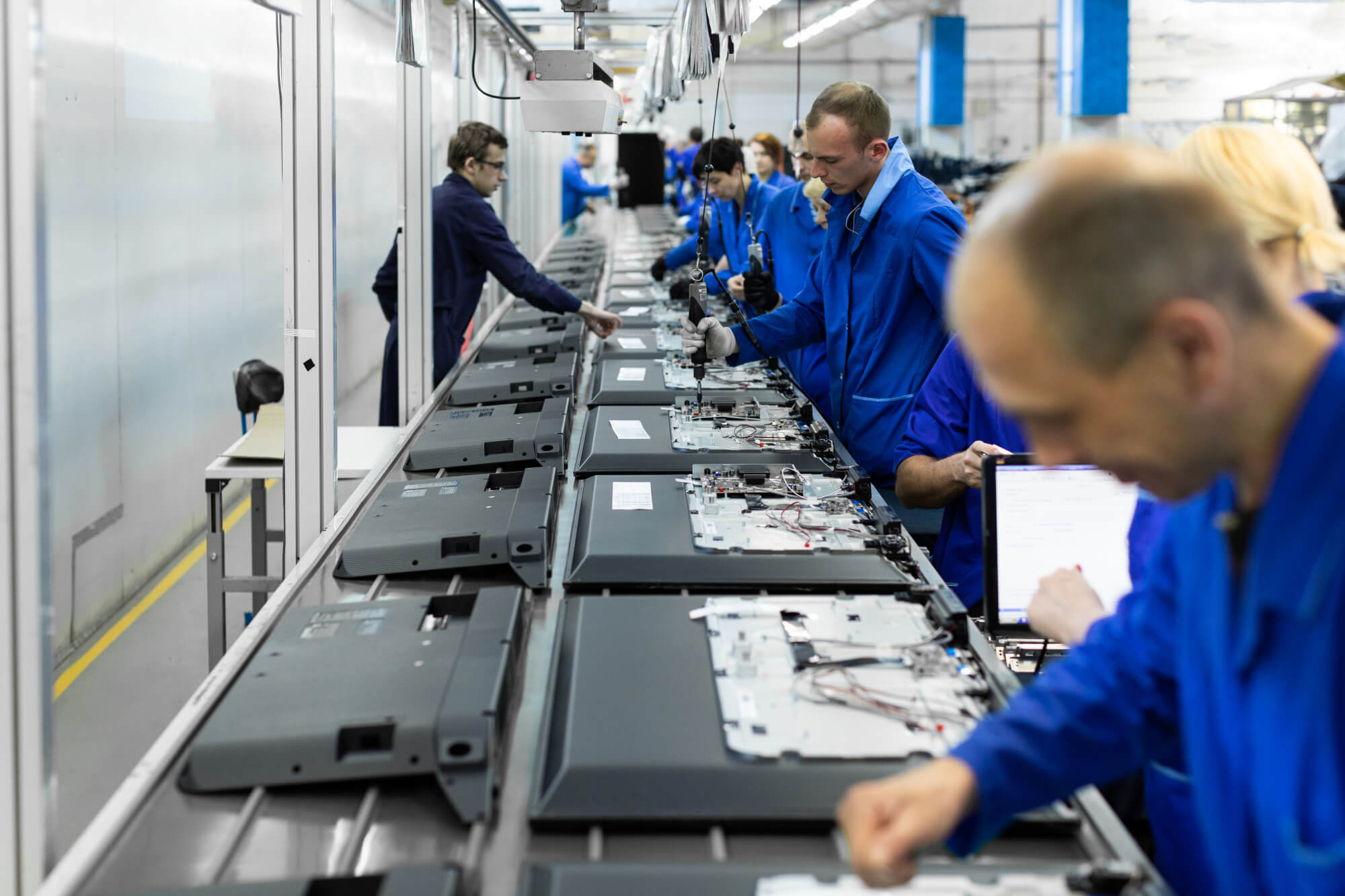 Workers in blue uniforms assembling electronics on a factory production line.