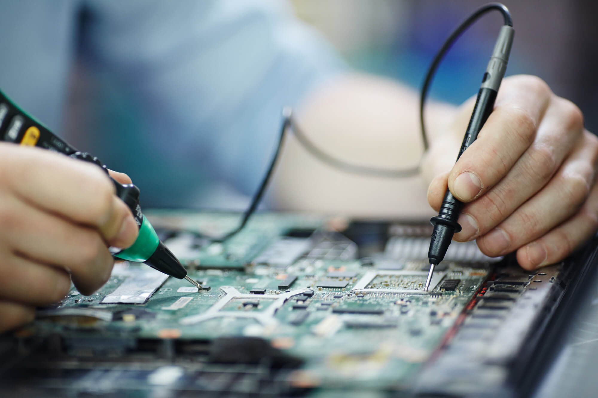 Hands using probes to test and diagnose components on a computer motherboard.