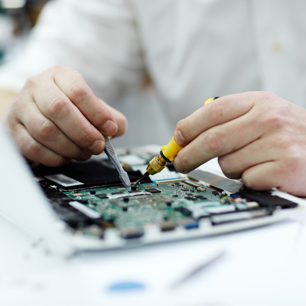 Person repairing a circuit board with a screwdriver and tweezers.