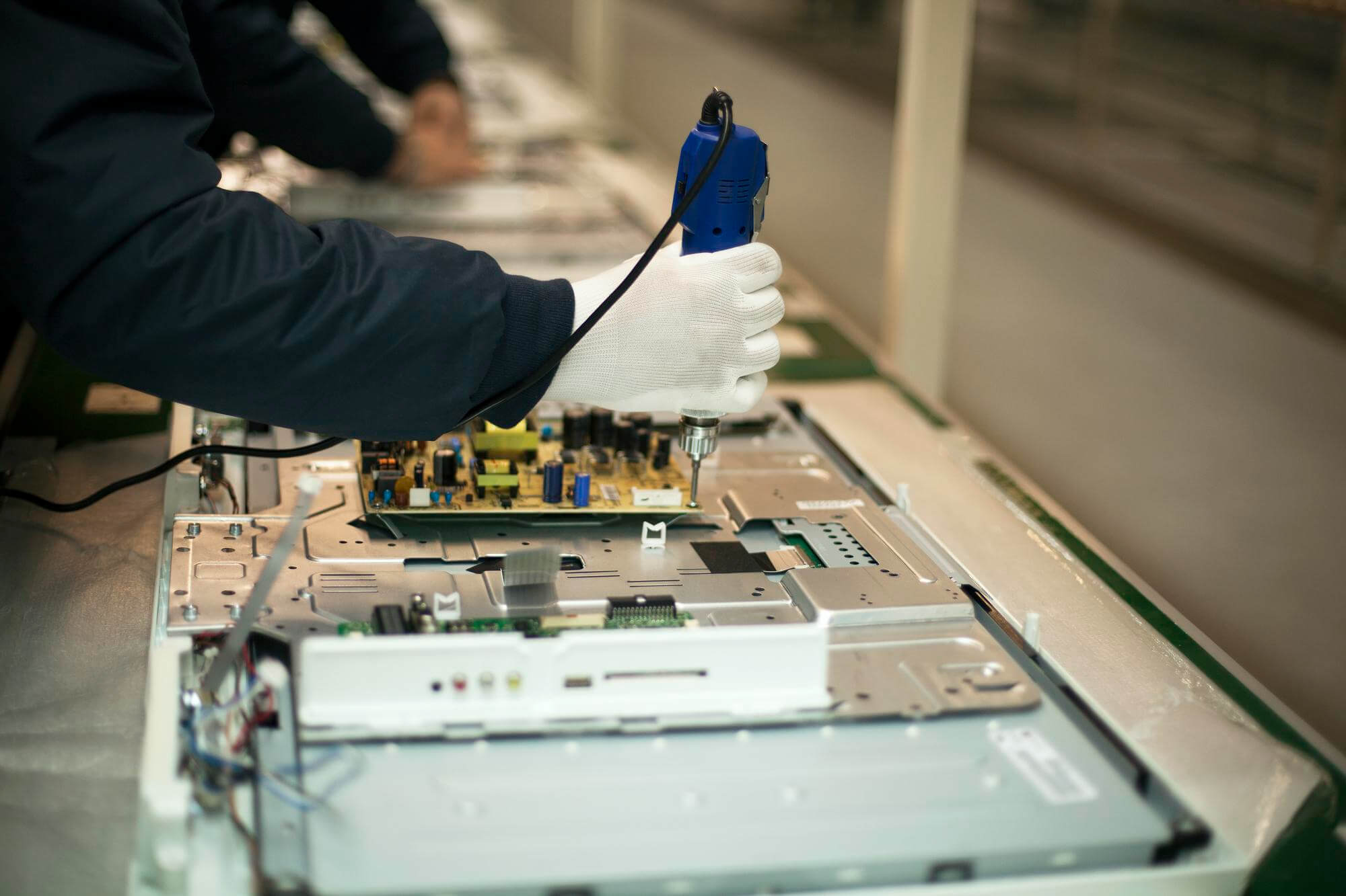 Technician wearing white gloves assembling or repairing electronic circuit board with a blue handheld tool.