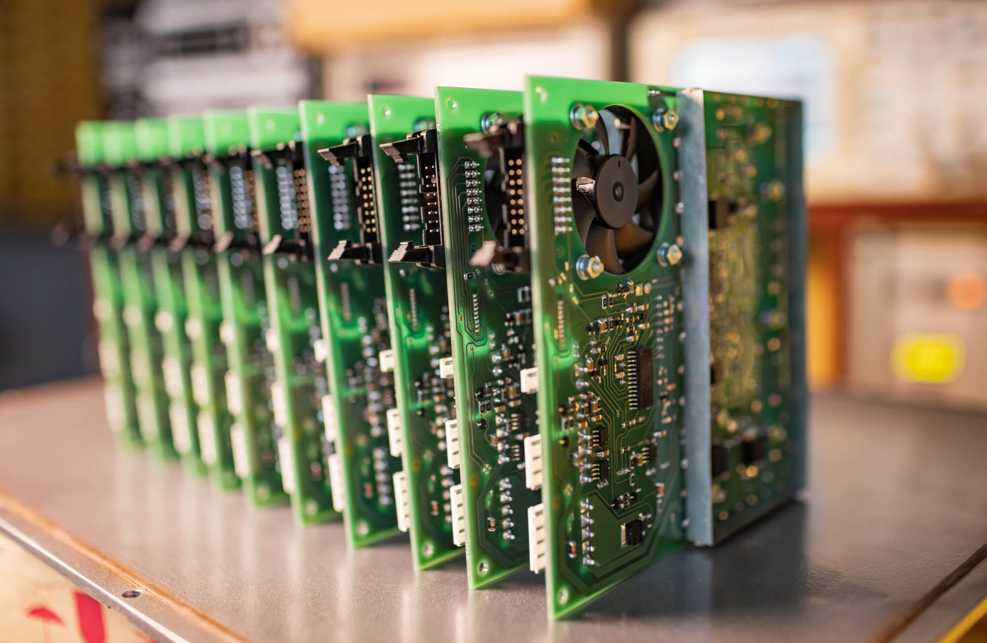 Row of green printed circuit boards with electronic components and cooling fans mounted vertically on a metal surface.