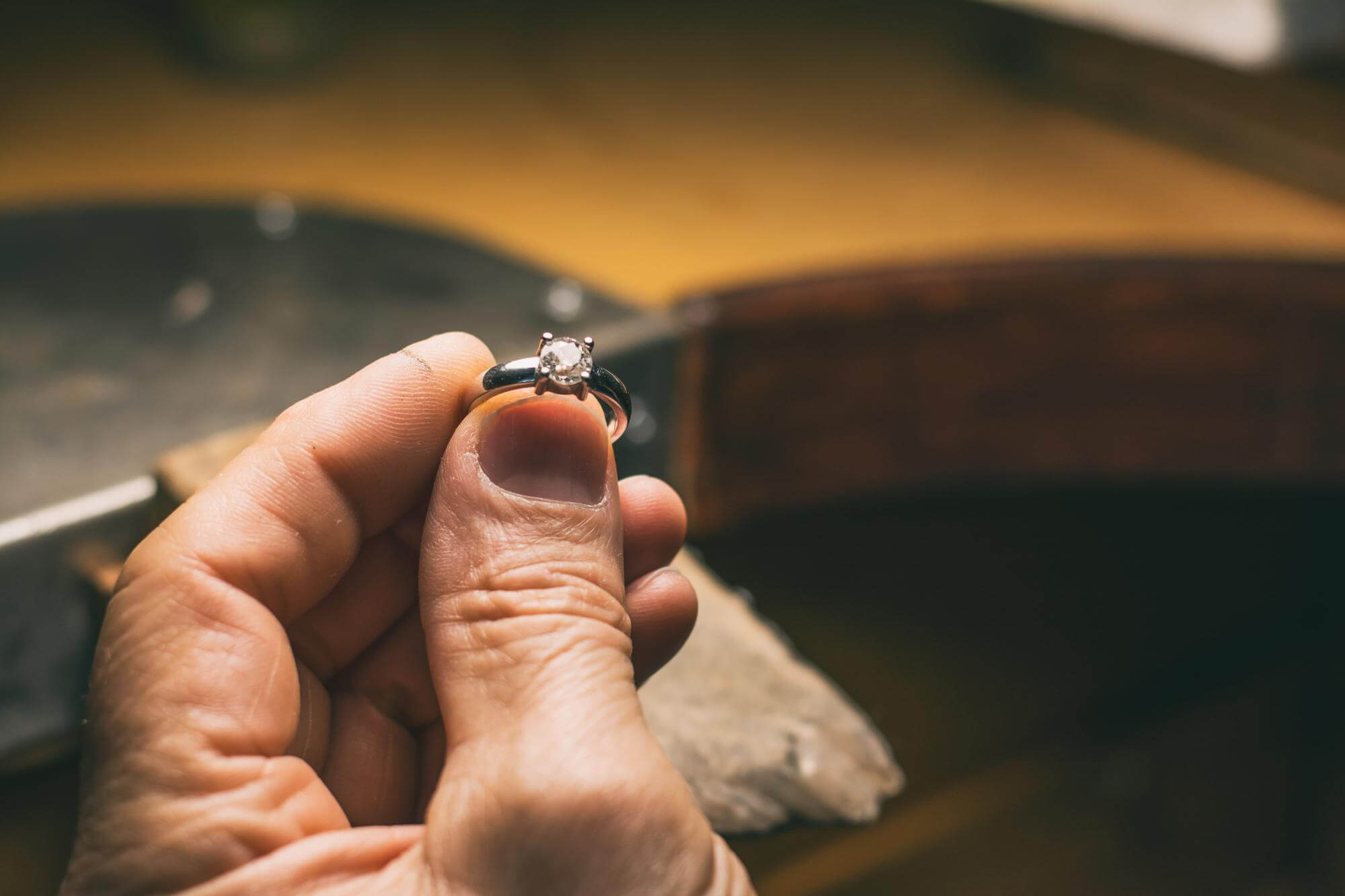Close-up of a hand holding a silver ring with a single round diamond in a jeweler's workshop.