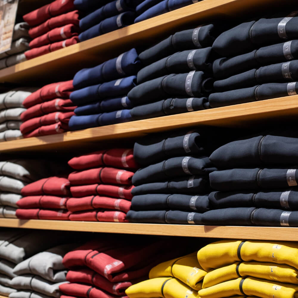 Shelves with neatly folded hoodies in colors black, red, navy blue, gray, and yellow organized by size labels.