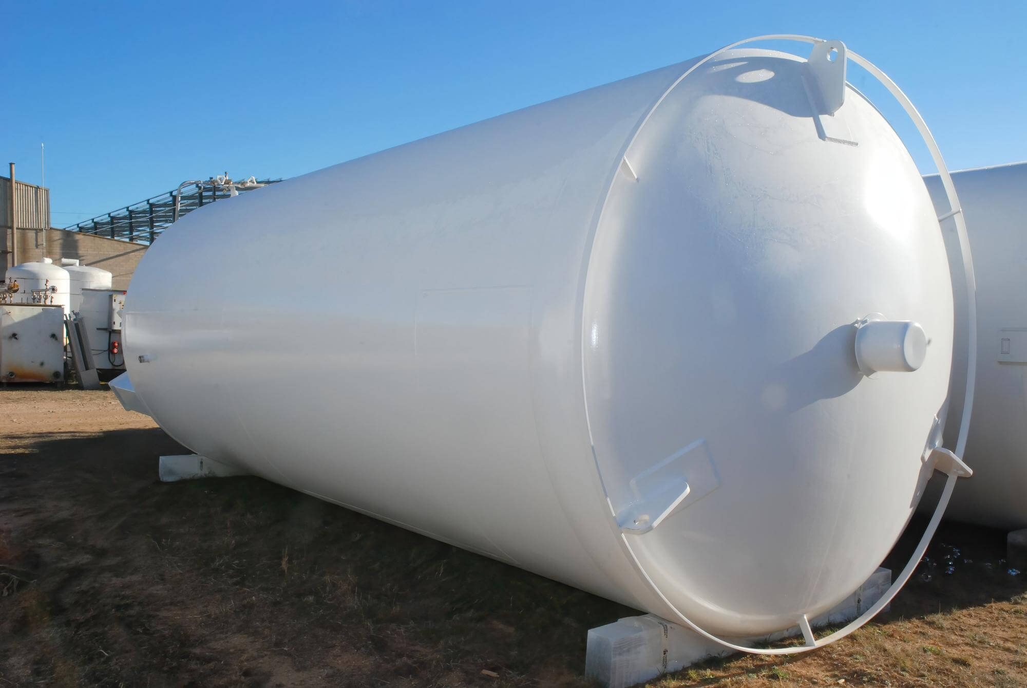 Large horizontal white industrial storage tank outdoors on blocks with a clear blue sky background.