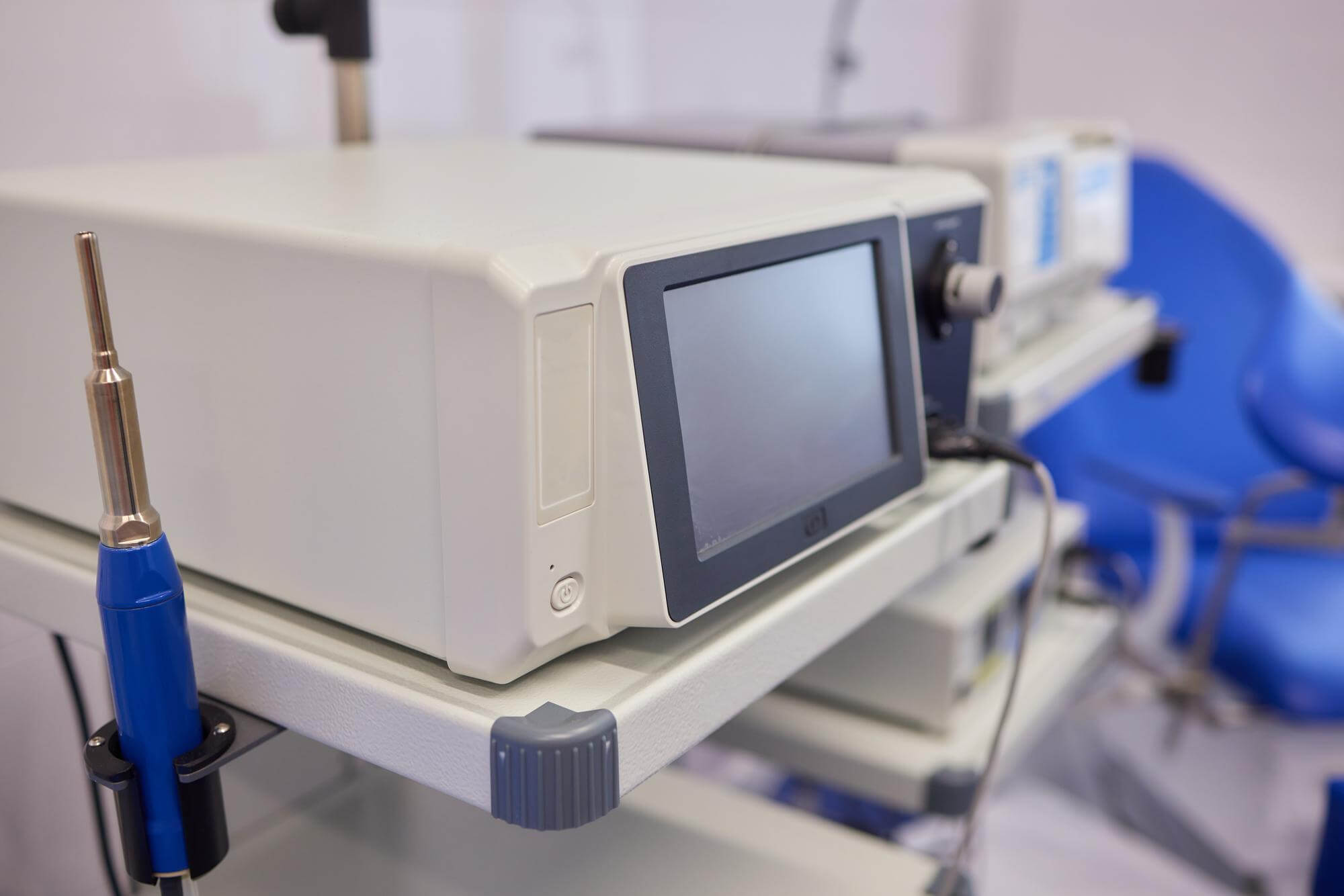 Close-up of medical diagnostic equipment with a display screen and a handheld probe attached on a cart in a clinical setting.