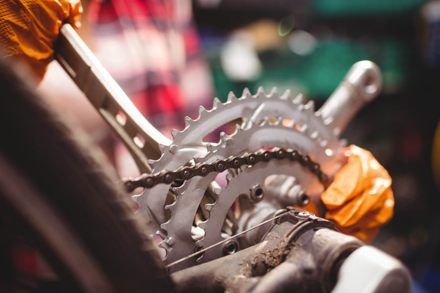 Close-up of a bicycle chain and gear system with a person wearing orange gloves working on it.