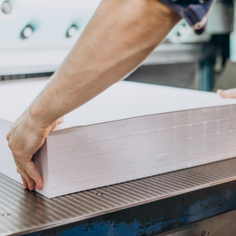 Hands holding a thick stack of white paper on a metal table surface.