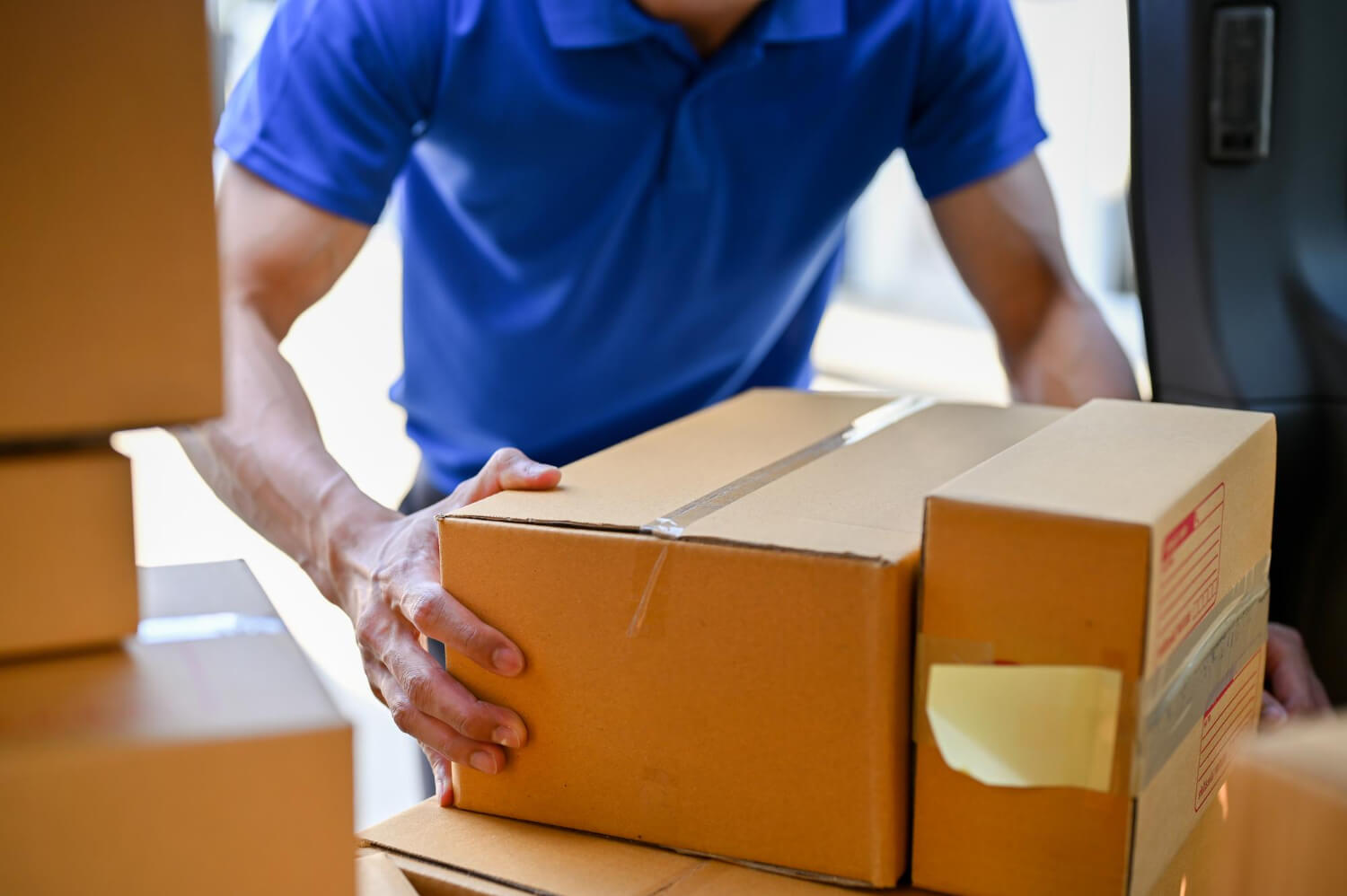Person in blue shirt loading or unloading cardboard boxes from a vehicle.