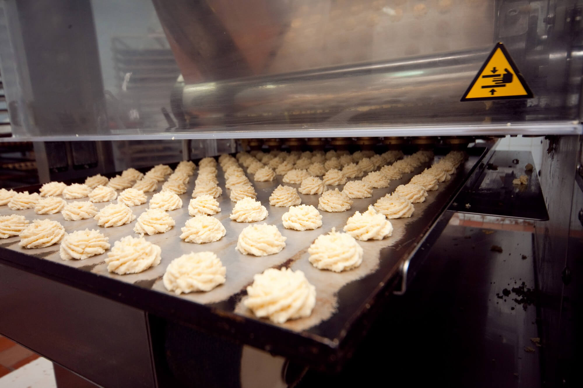 Rows of piped dough or batter on a baking tray inside an industrial oven.