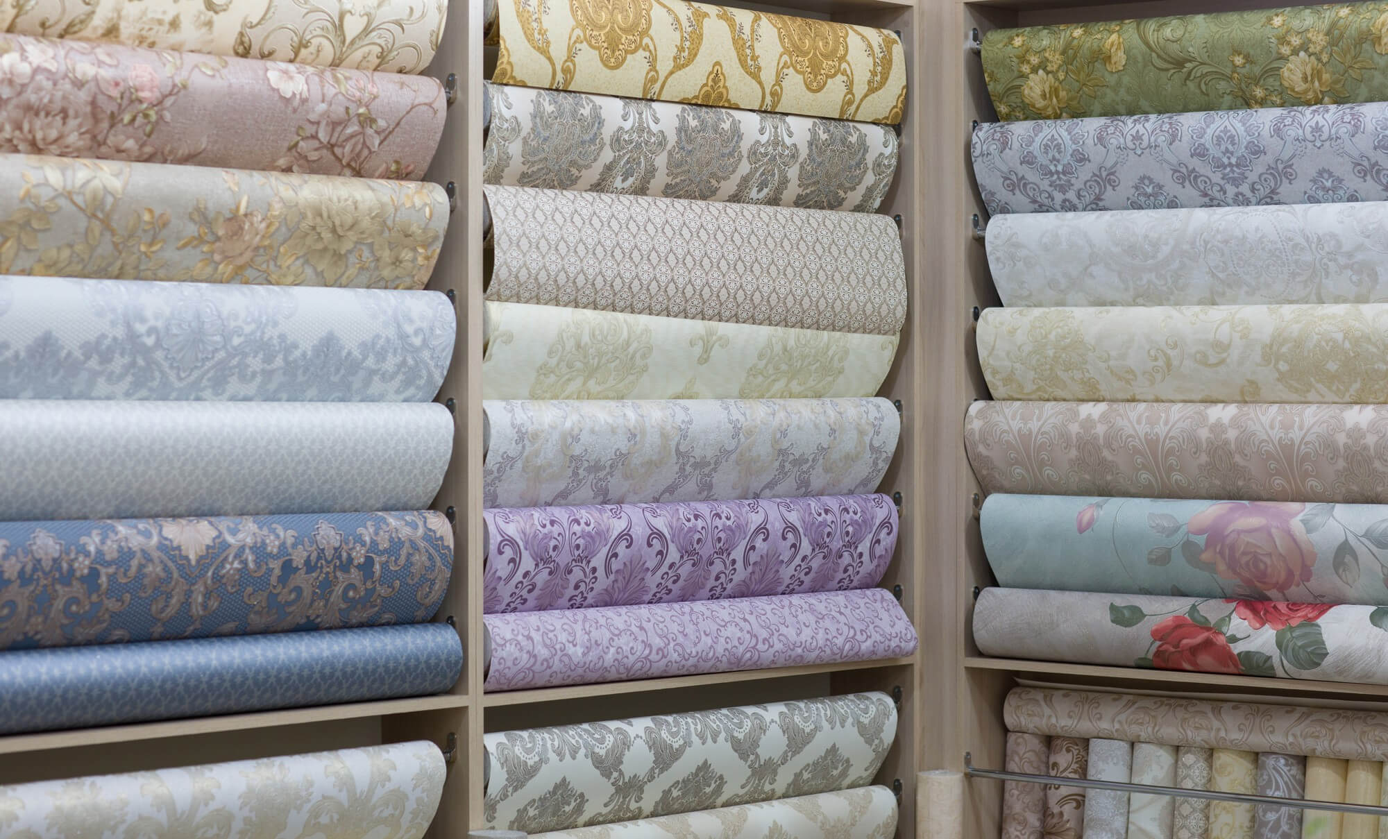 Shelves displaying various rolls of floral and patterned wallpaper in pastel and muted tones.