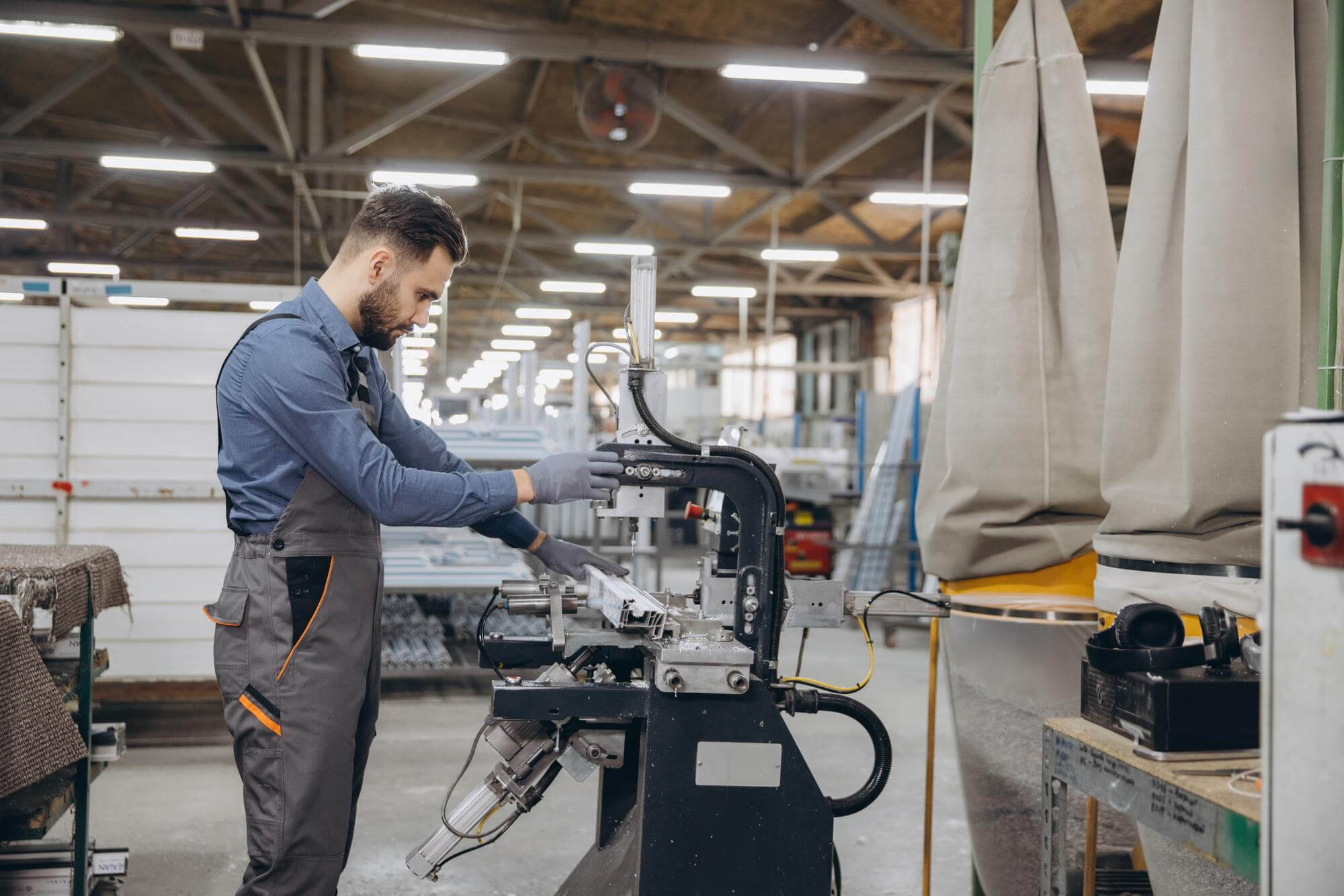 Worker in gray overalls operating industrial machinery in a spacious factory setting.