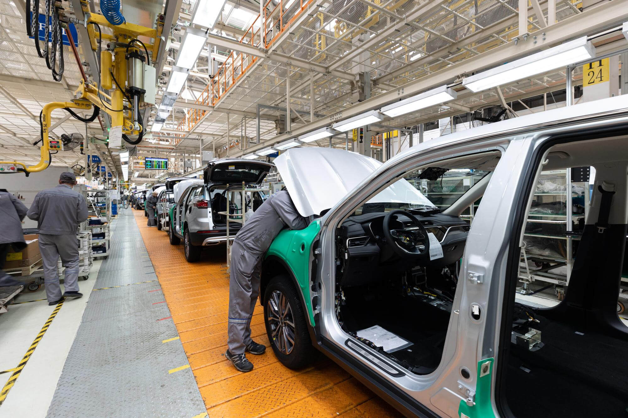 Workers assembling silver cars on an automotive production line inside a factory.
