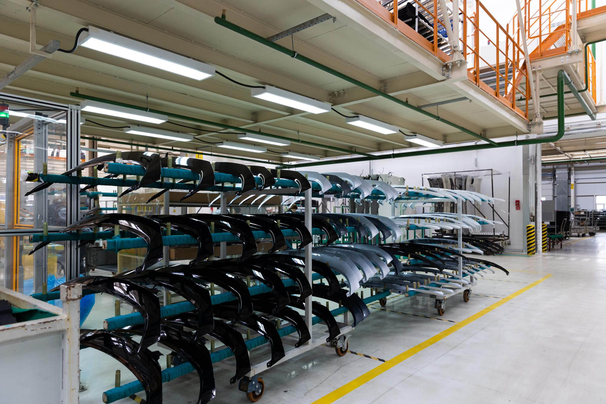 Shelves with black and white car bumpers lined up inside a clean automotive factory.