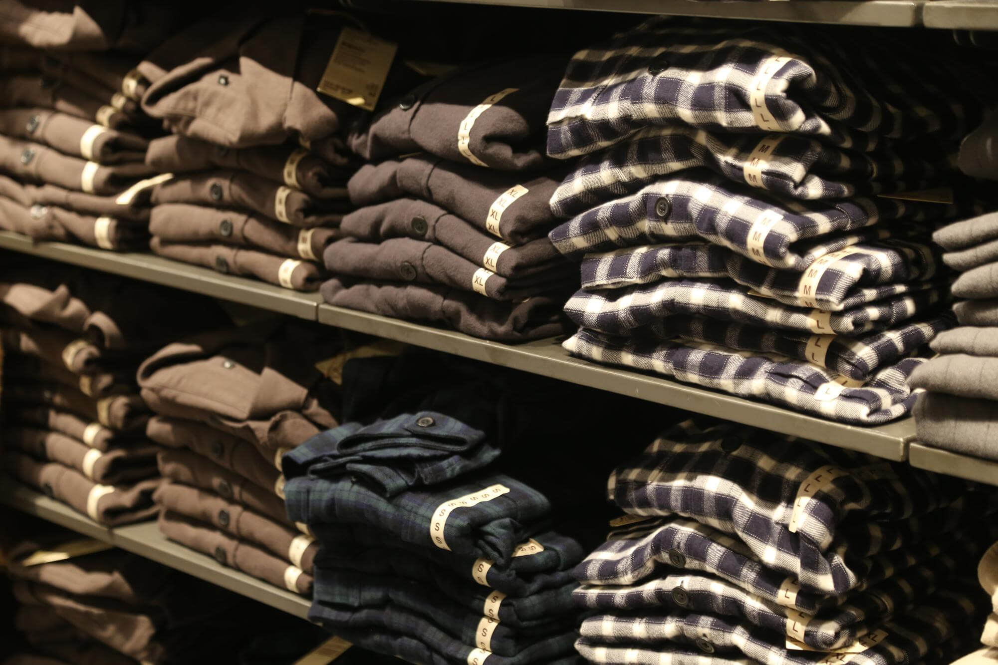 Shelves filled with neatly folded brown, navy, and blue checkered shirts organized by size labels.