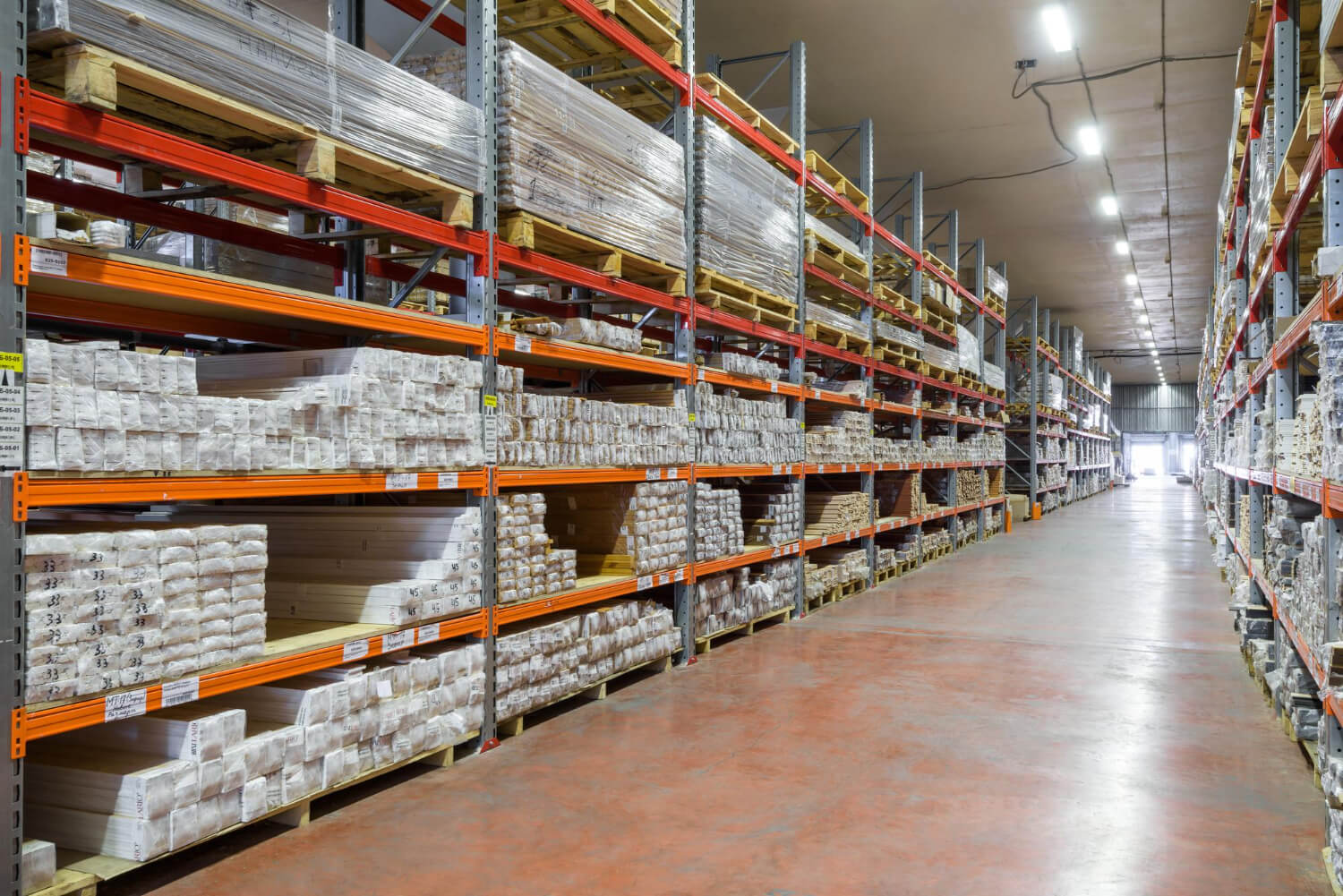 Long aisle of warehouse shelves stocked with bundled and palletized construction materials.