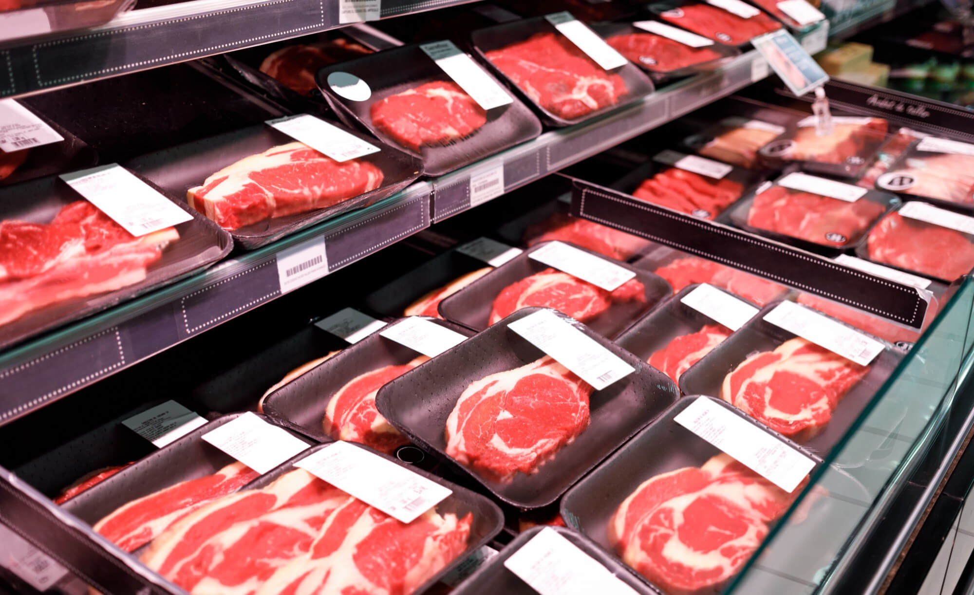 Store display case with multiple packages of raw beef steaks in black trays with white labels.