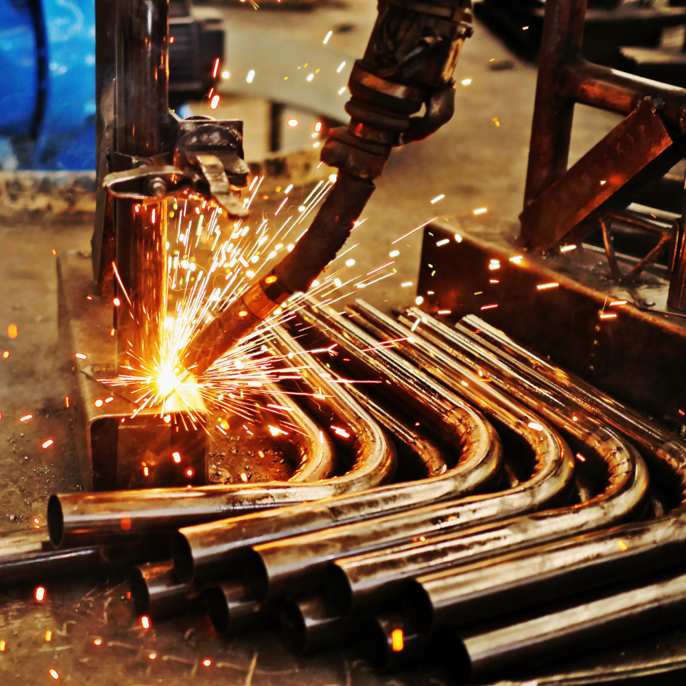 Close-up of welding torch cutting or welding metal pipes with bright sparks flying.