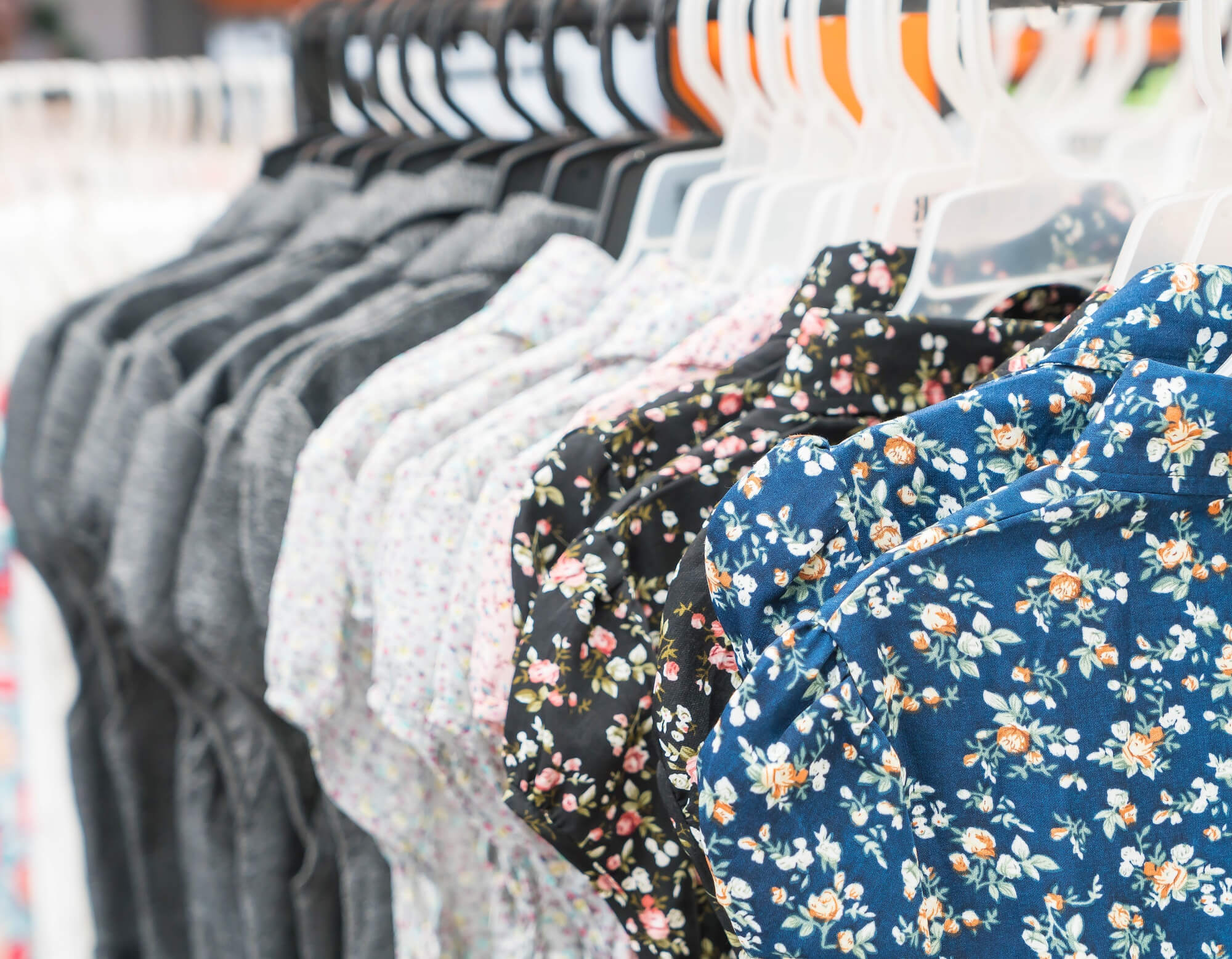 Row of floral and patterned shirts hanging on hangers in a clothing store.