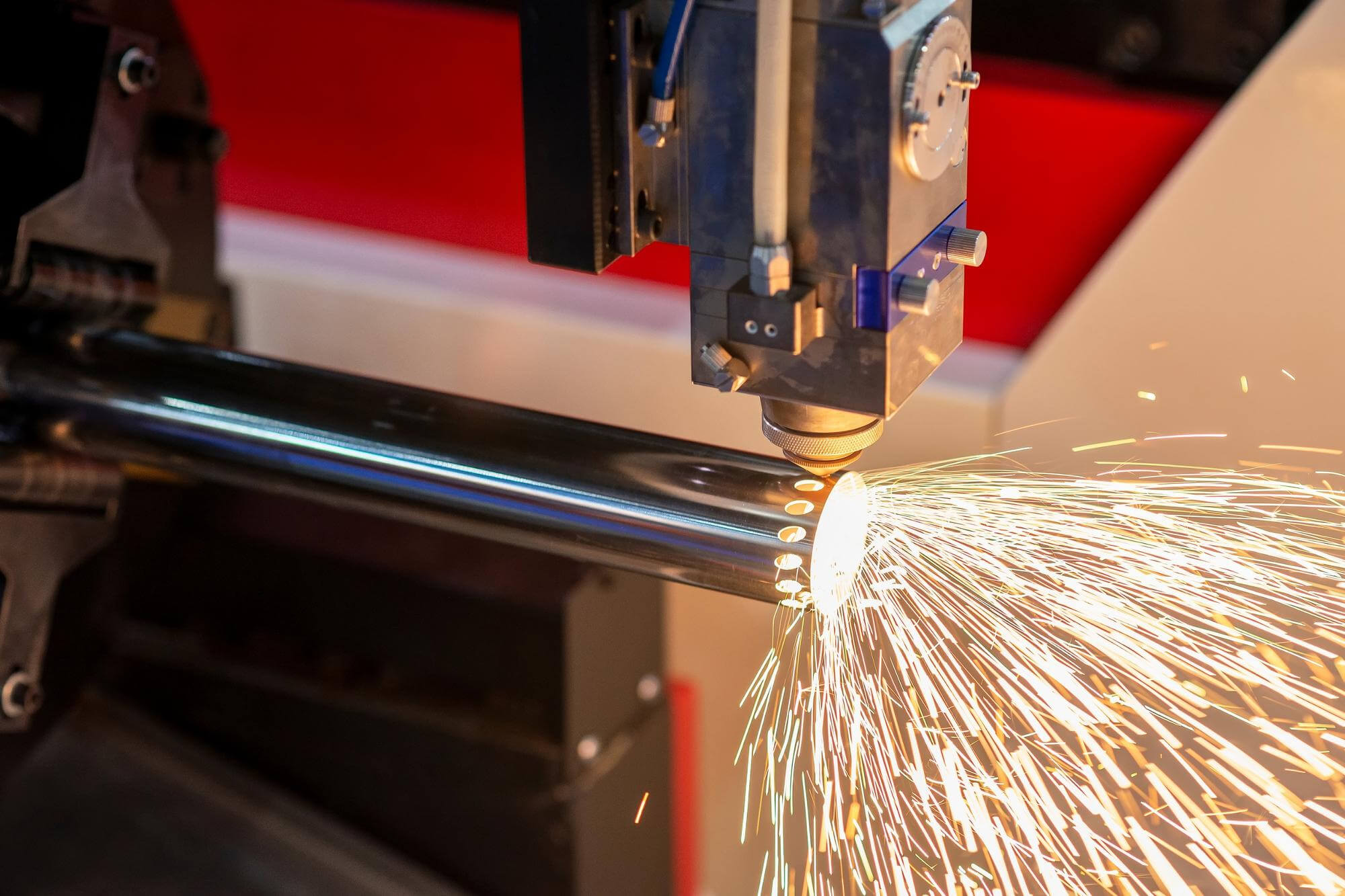 Laser cutting machine generating sparks while cutting holes in a metal pipe.