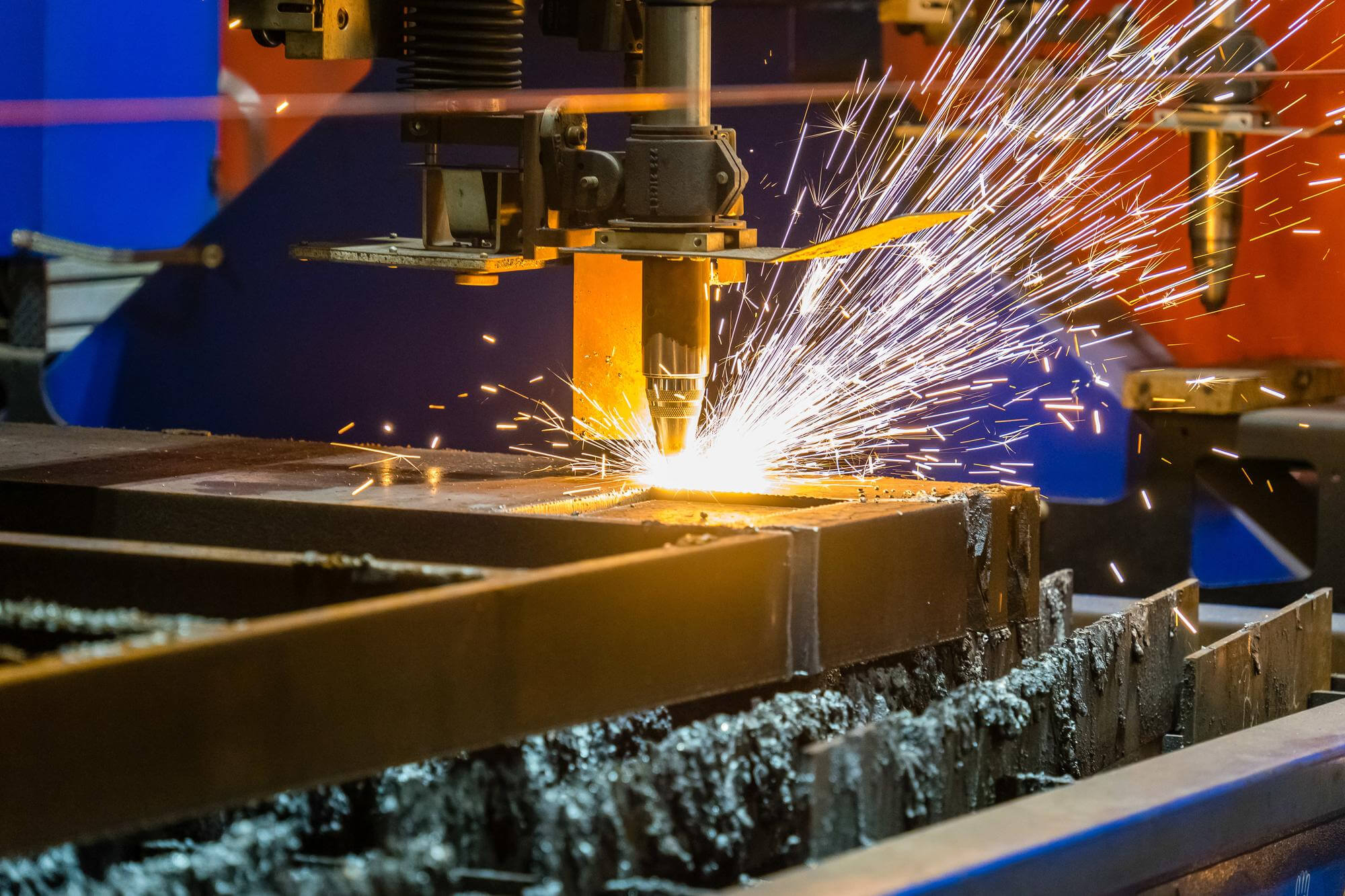 Industrial metal cutting machine producing bright sparks while cutting thick steel sheet.