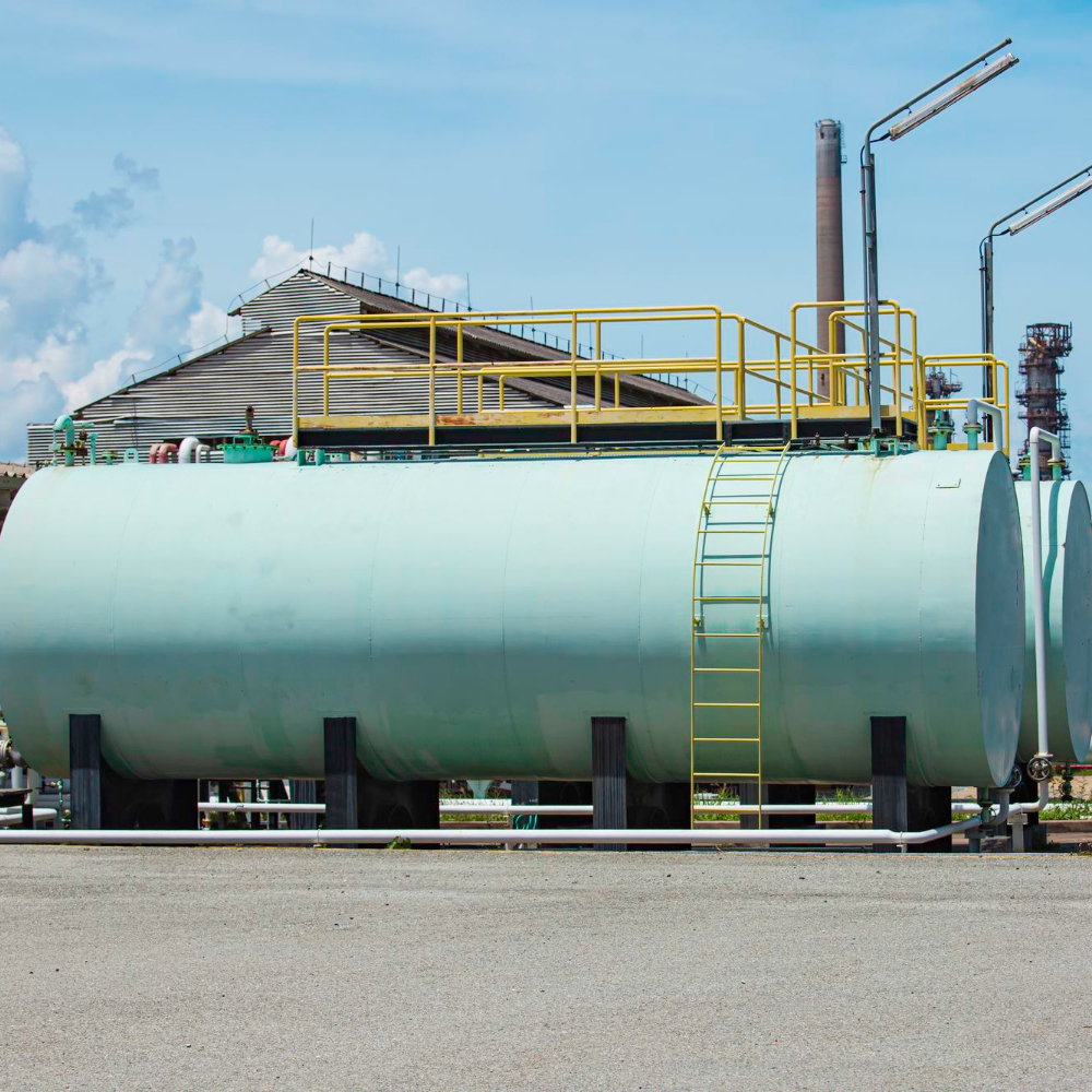 Large industrial storage tank with yellow safety railing and ladder at a refinery plant under blue sky.