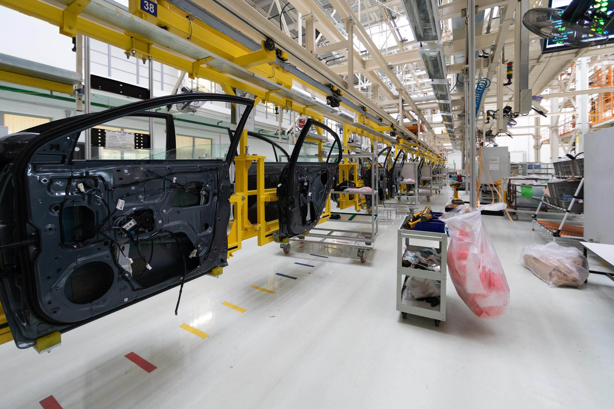 Car doors hanging on a yellow overhead conveyor system in a modern automotive assembly line.