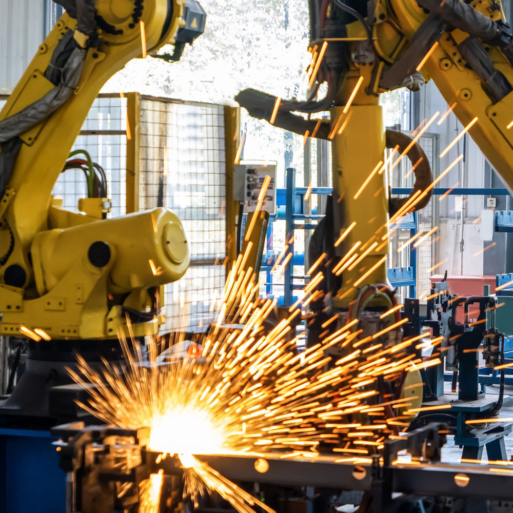 Yellow industrial robotic arms welding metal with sparks flying inside a factory.