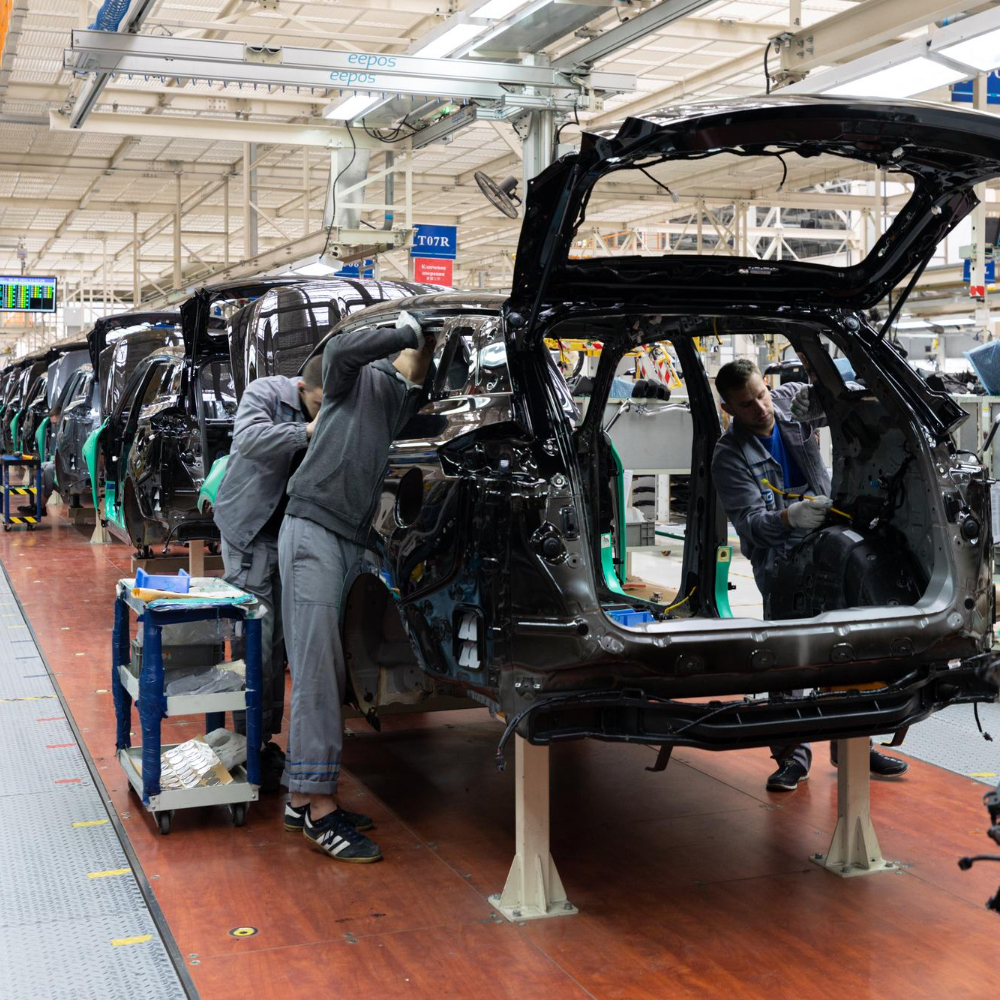 Workers assembling black car bodies on an automotive production line inside a factory.
