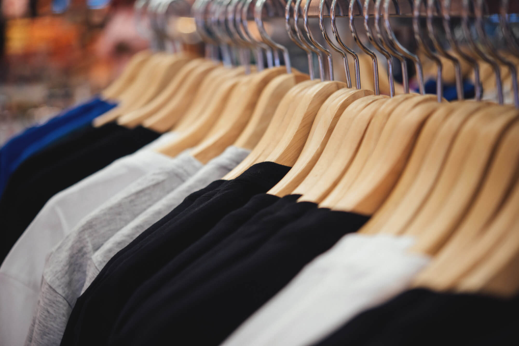 Row of black, white, gray, and blue shirts hanging on wooden hangers in a retail store.