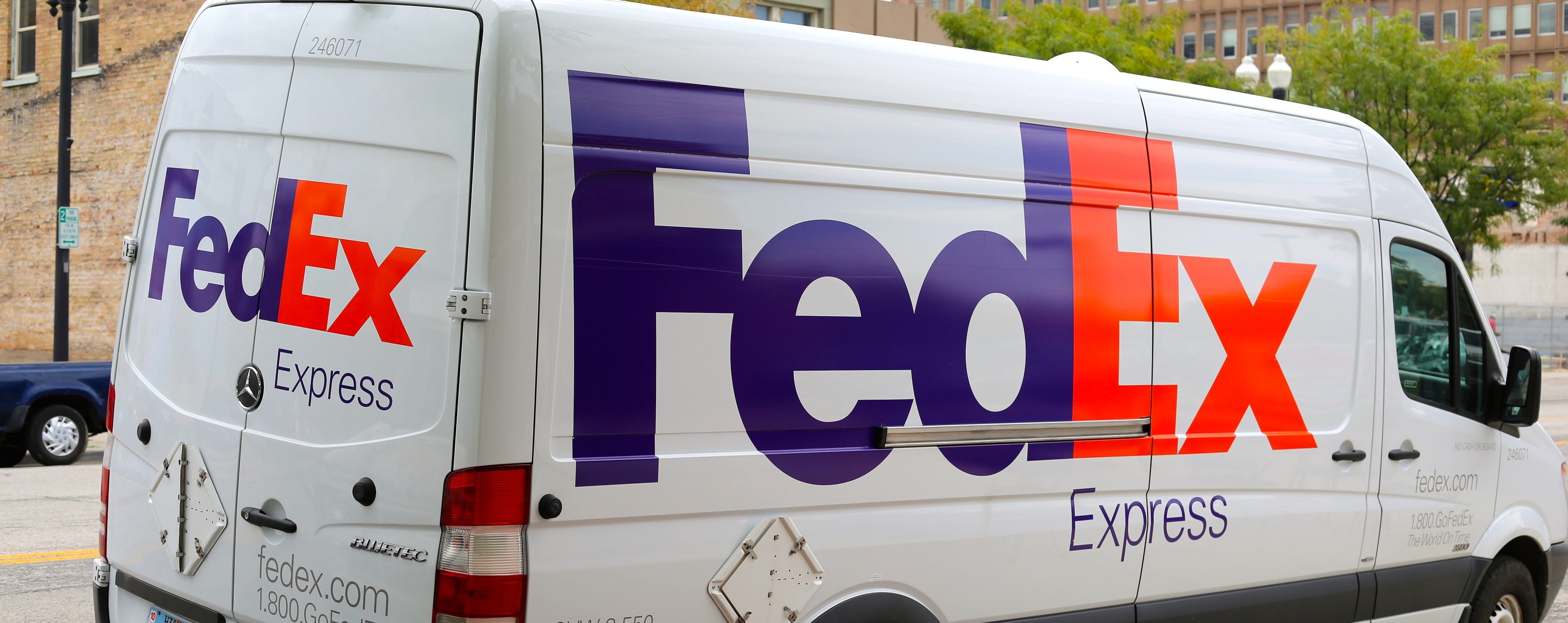 White FedEx Express delivery van with purple and orange logo parked on an urban street.