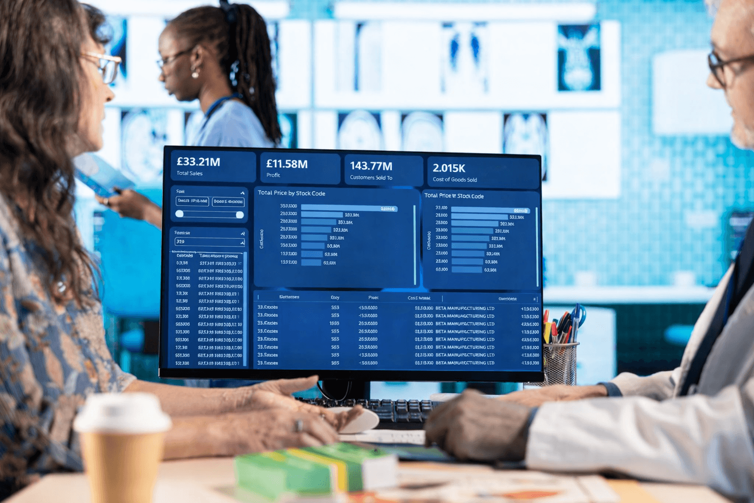 Two professionals, a woman and a man, discussing data displayed on a computer screen showing financial metrics and charts in an office.